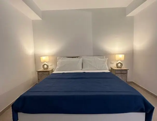 Letto matrimoniale con coperte blu e cuscini bianchi in camera luminosa a Nova Siri